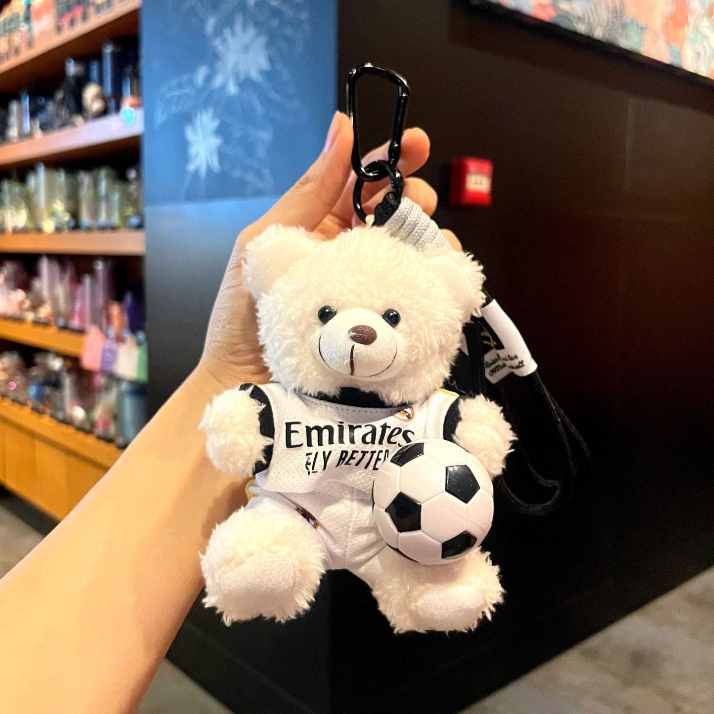 White plush bear keychain in white jersey with black graphics, holding a soccer ball