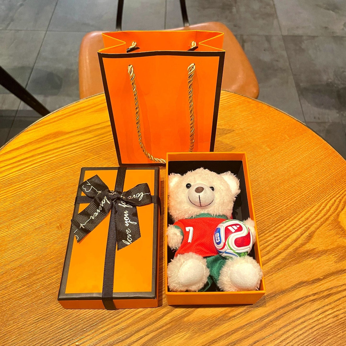 Orange gift bag and box set with white plush bear keychain in red soccer jersey and soccer ball