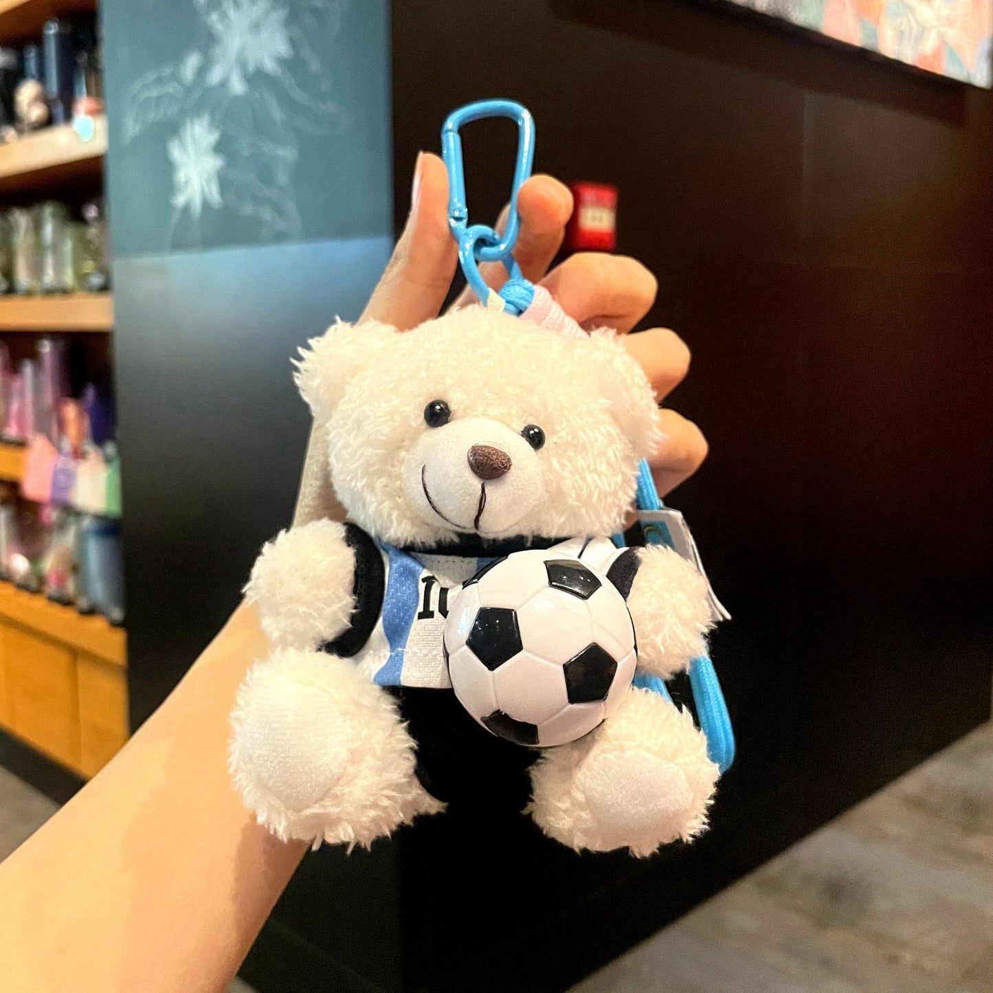White plush bear keychain with blue clip, wearing blue soccer jersey, holding a soccer ball