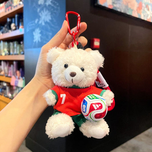 White plush bear keychain in red soccer jersey with green shorts, holding a soccer ball