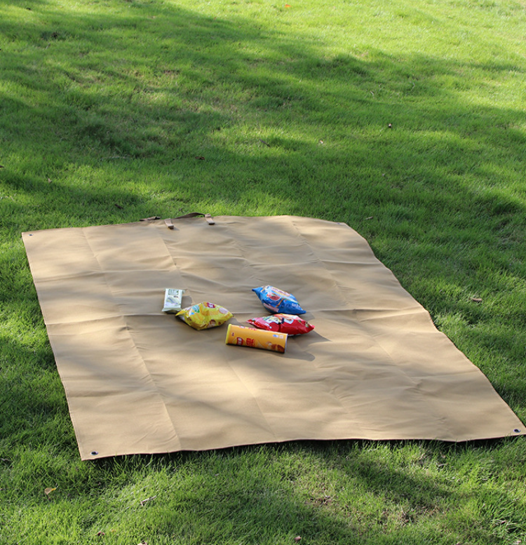 Khaki waterproof picnic mat laid flat on grass with snack packages on top