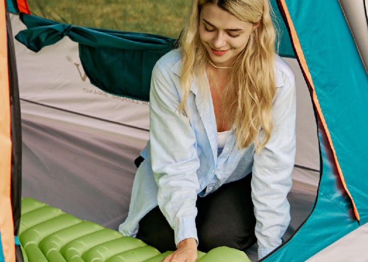 Emerald green inflatable camping sleeping pad with built-in pillow, person smoothing surface