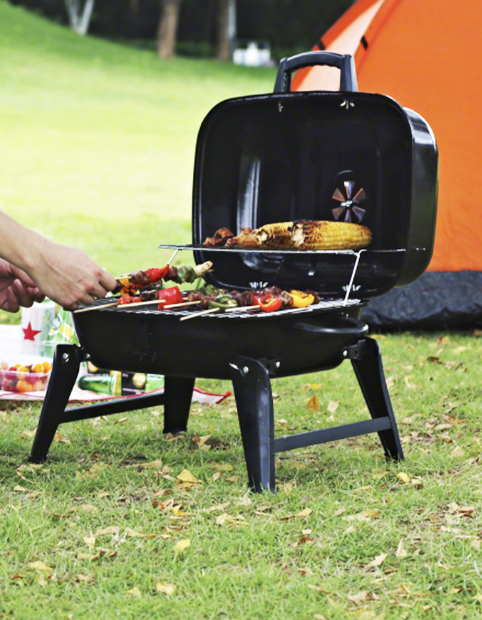 Black portable foldable charcoal grill with lid open, corn and vegetables on grate