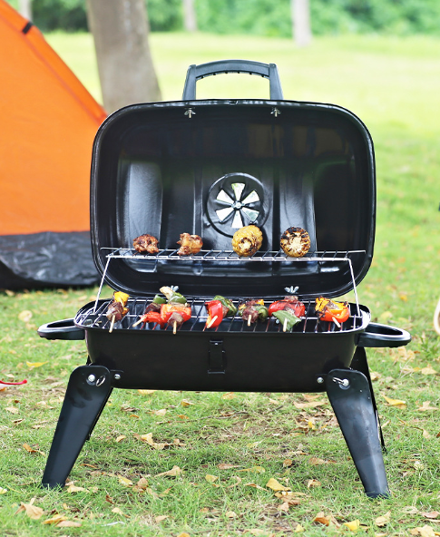 Black portable foldable charcoal grill with lid open, kebabs and vegetables on grate
