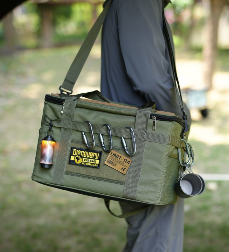Green tactical camping storage bag with front pockets, carabiner clips, and shoulder strap.