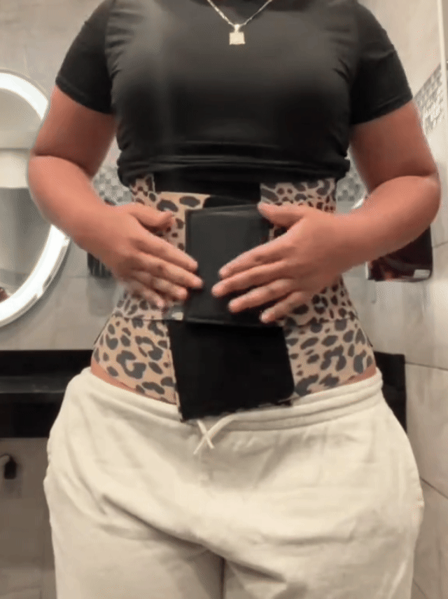Black triple-wrap waist trainer belt being adjusted with hook-and-loop closure