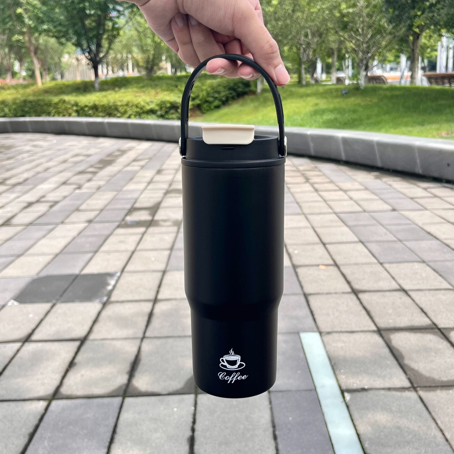 Portable stainless steel insulated bottle, black, held by handle
